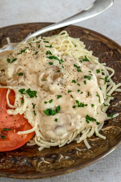 slow cooker chicken parisienne over pasta with sliced tomatoes on the side