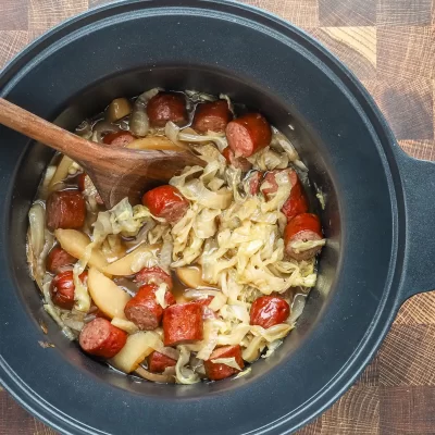Sliced sausages with cooked cabbage and onions simmered in a slow cooker.
