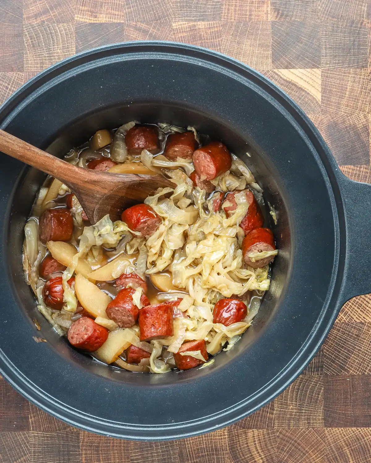 Sliced sausages with cooked cabbage and onions simmered in a slow cooker.