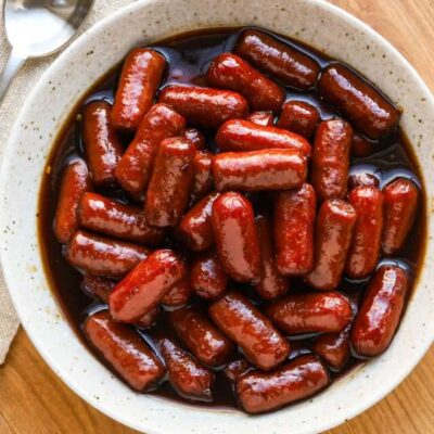 Sweet glazed sausages with rich sauce in a white bowl.