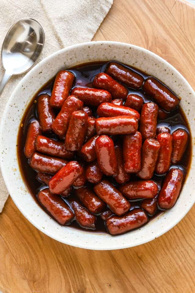 Sweet glazed sausages with rich sauce in a white bowl.