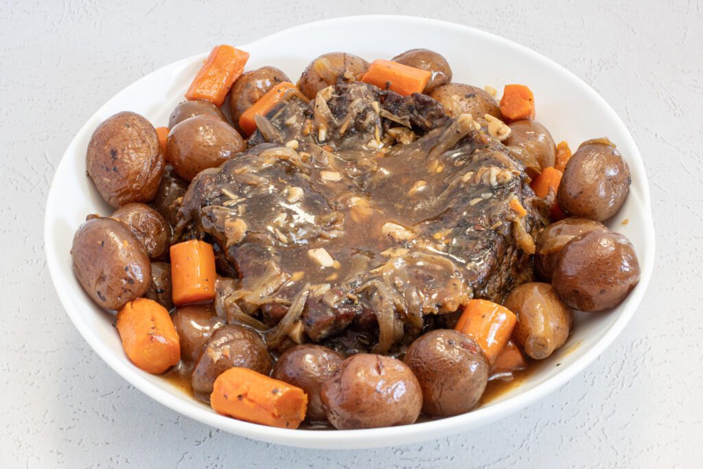 slow cooker pot roast in a serving dish with potatoes, carrots, and gravy.
