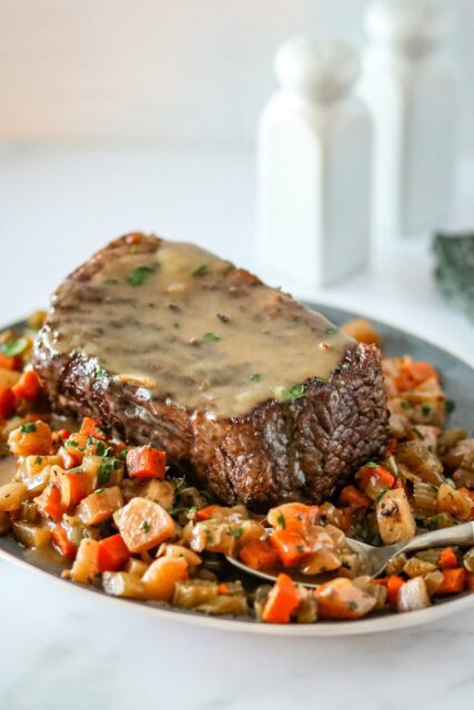 slow cooker pot roast and gravy surrounded by diced vegetables.