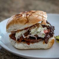 A slow cooker shredded beef sandwich with coleslaw and BBQ sauce.