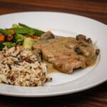 pork chop and gravy on a plate with rice and vegetables