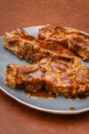 Baked pork ribs glazed with barbecue sauce on a gray plate.