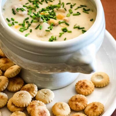A bowl of tuna and corn chowder with oyster crackers on the plate.