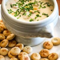 A bowl of tuna and corn chowder with oyster crackers on the plate.