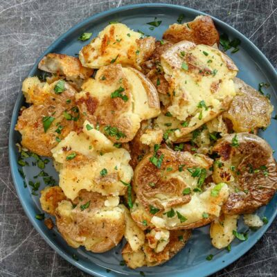 Fried smashed potatoes in a plate with garnish.
