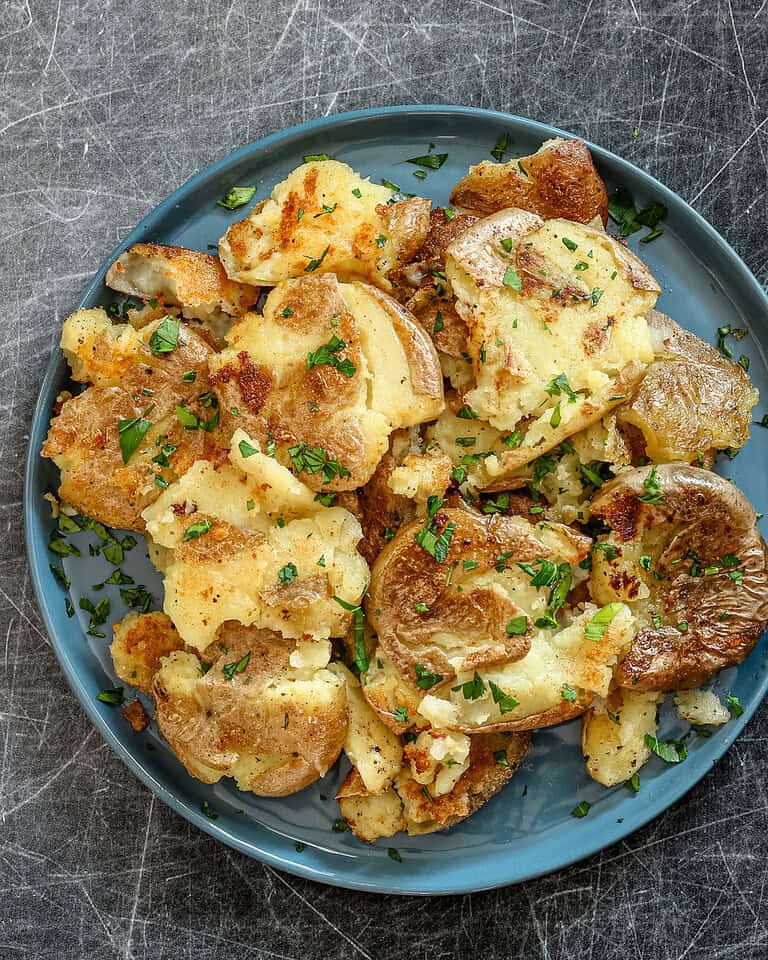 Fried smashed potatoes in a plate with garnish.
