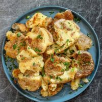 Fried smashed potatoes in a plate with garnish.