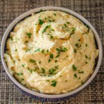 a serving bowl with parsley-garnished smoked cheddar mashed potatoes