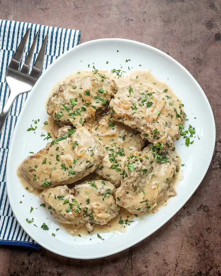 Creamy chicken with herbs and mushroom gravy served on a white plate.