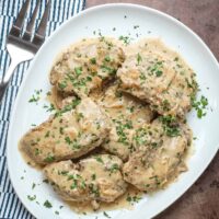 A serving platter with boneless pork chops smothered with a tasty onion gravy, garnished with parsley.