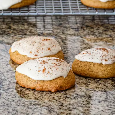 Pumpkin cookies on the counter with more in the background.