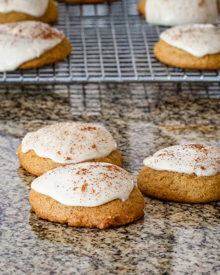 Pumpkin cookies on the counter with more in the background.