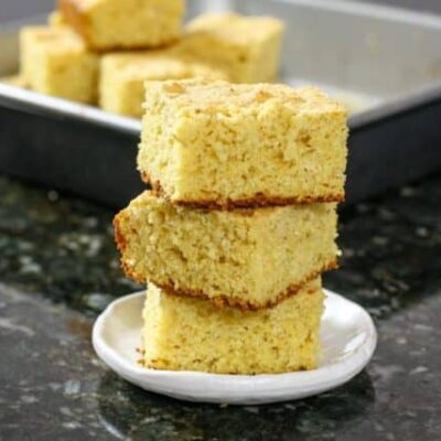 sour cream cornbread squares stacked with the pan in the background