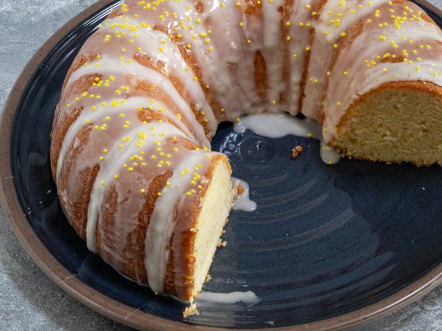 sour cream lemon cake on a cake plate with glaze and sprinkles