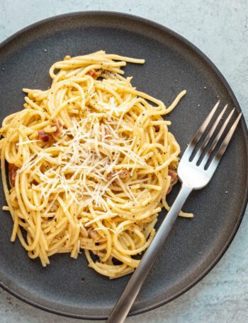 spaghetti carbonara on a plate with fork and parmesan cheese topping
