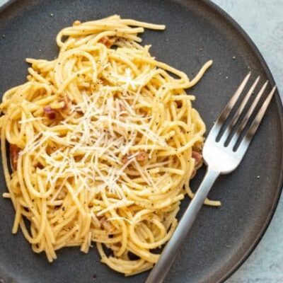 spaghetti carbonara on a plate with fork and parmesan cheese topping