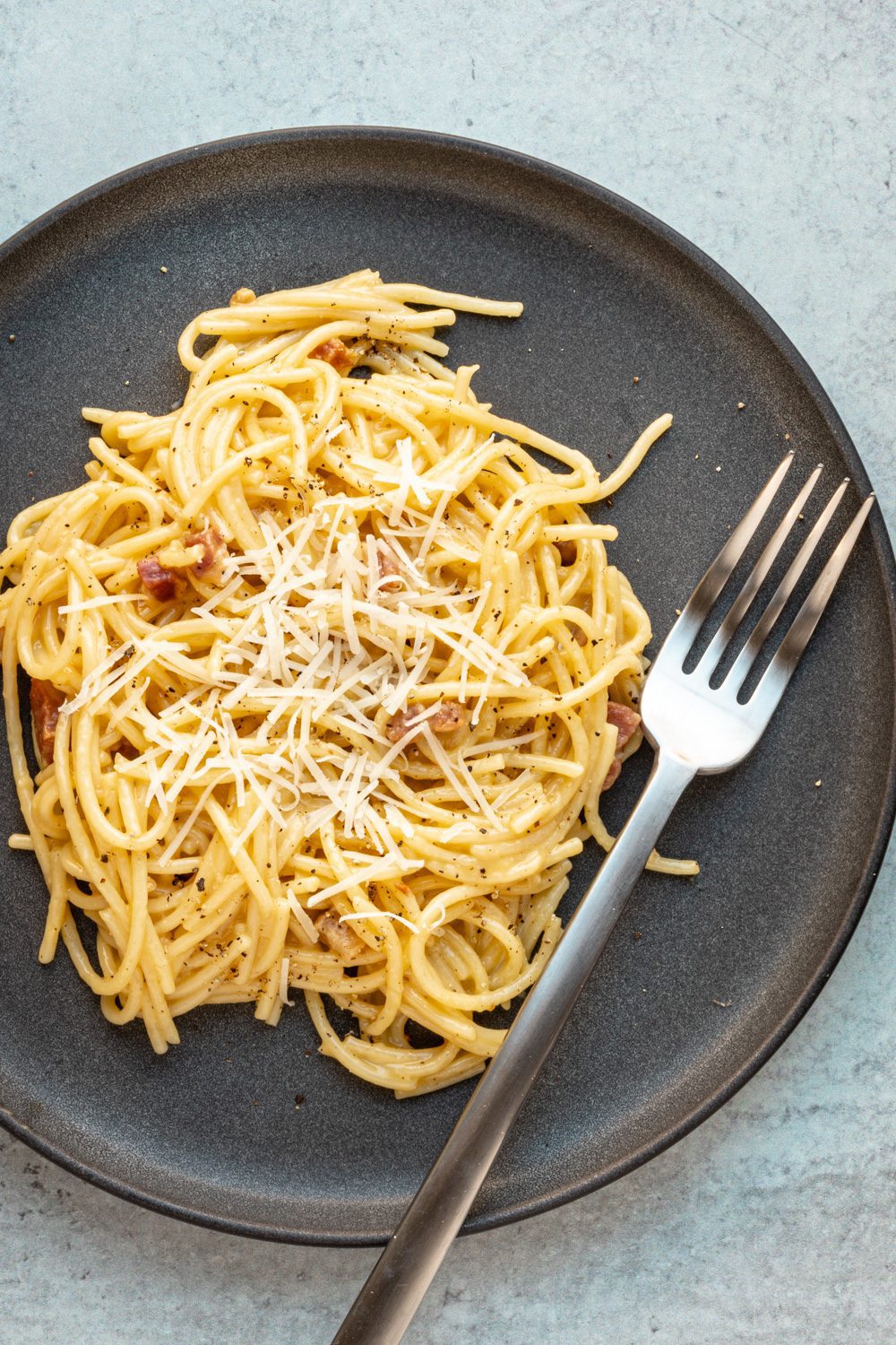 spaghetti carbonara on a plate with fork and parmesan cheese topping