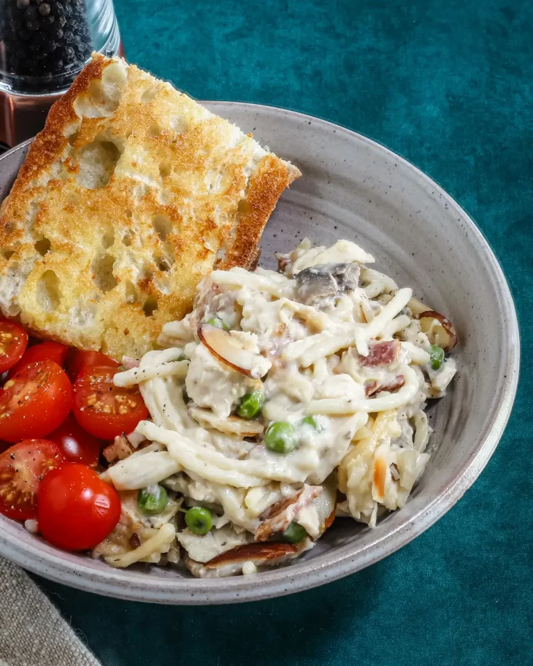 Chicken tetrazzini in a bowl with toasted garlic bread and sliced tomatoes.