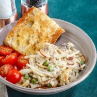 Creamy chicken alfredo with peas, cherry tomatoes, and a toasted garlic bread slice in a bowl.