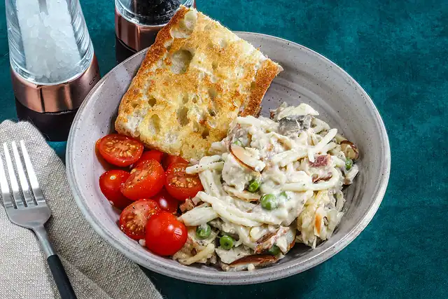 A bowl of quick chicken tetrazzini with garlic bread and tomatoes on the side.
