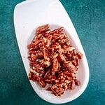 Cooked bacon pieces on a white plate over a teal background.