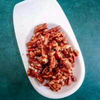 Cooked bacon pieces on a white plate over a teal background.