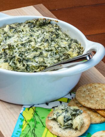 spinach artichoke dip in a baking dish with crackers on the side