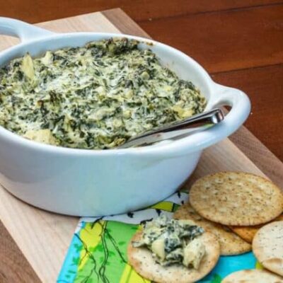 spinach artichoke dip in a baking dish with crackers on the side