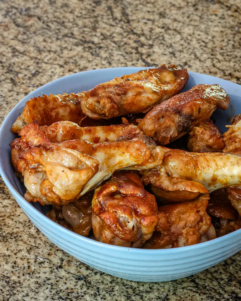 Fried chicken drumsticks in a blue bowl on a speckled countertop.