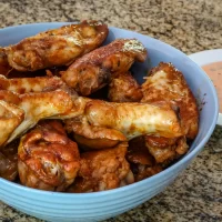 Fried chicken wings coated in spicy sauce in a blue bowl on a granite countertop.