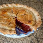 a baked strawberry rhubarb pie with 1 slice missing