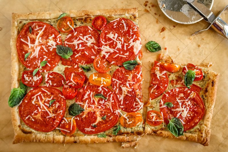a baked tomato tart on a puff pastry and pesto-cream cheese base