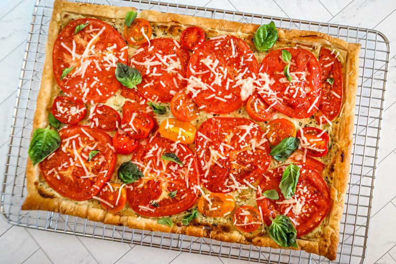 a baked tomato tart on a puff pastry and pesto-cream cheese base on a cooling rack