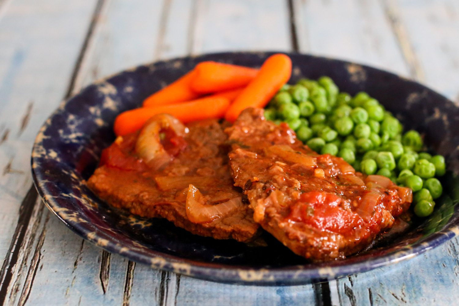 swiss steak on a plate with carrots and peas