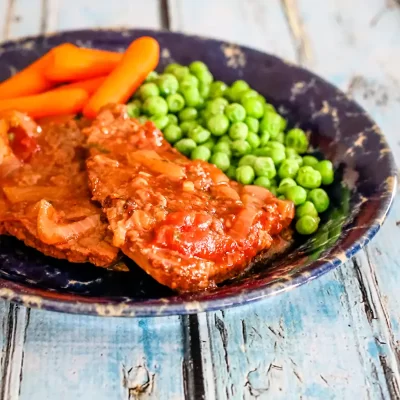Fresh cooked meat with peas and carrots on a rustic plate.