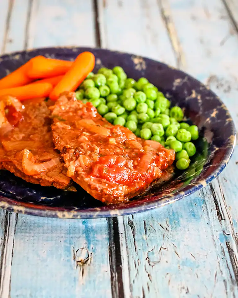 Fresh cooked meat with peas and carrots on a rustic plate.