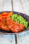 Juicy pot roast with carrots and green peas on rustic plate.