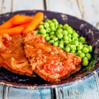 Succulent meat with a rich sauce served with peas and carrots on a rustic plate.