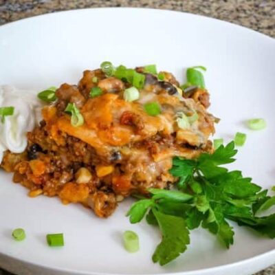 layered tamale casserole with ground beef on a plate with herbs, sour cream, and green onions