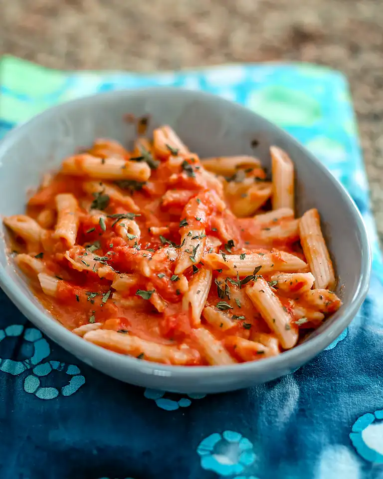 Pasta with tomato sauce and fresh herbs in a gray bowl.