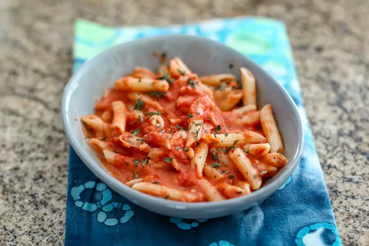 Penne pasta with tomato sauce topped with chopped herbs in a bowl over a blue napkin.
