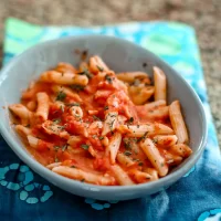 Pasta with tomato sauce and chopped herbs in a gray bowl.