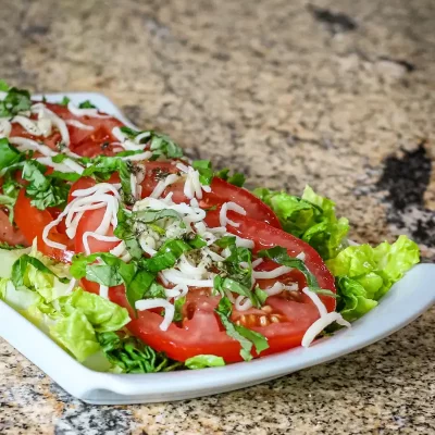 Fresh tomato and lettuce salad topped with shredded cheese and chopped herbs.