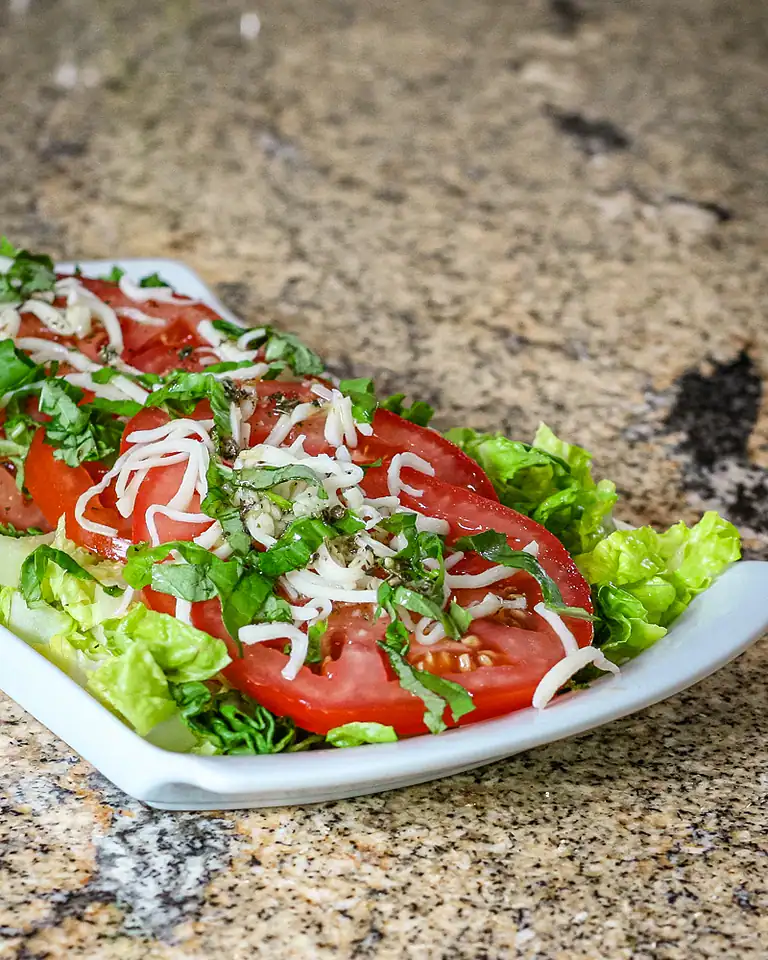 Fresh tomato and lettuce salad topped with shredded cheese and chopped herbs.