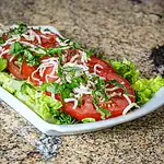 Fresh tomato and shredded cheese salad on a white plate.
