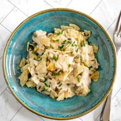 Creamy potato salad with peas and chopped chives on blue ceramic plate.